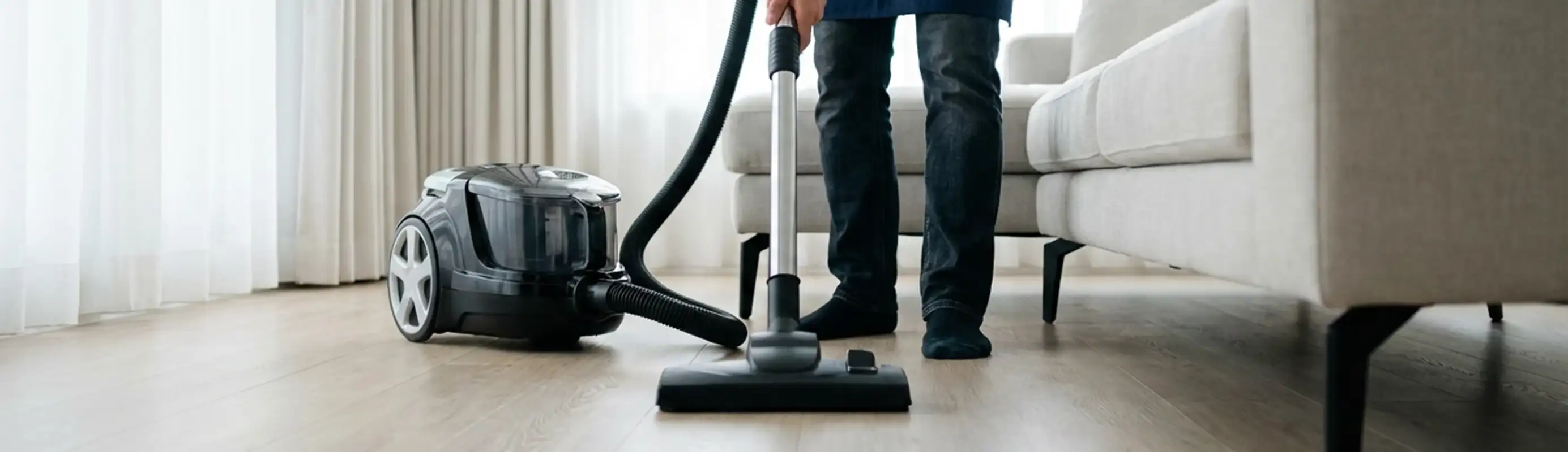 Professional house cleaner vacuuming a living room floor with a canister vacuum cleaner, Rochester, NY.