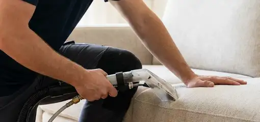 Professional upholstery cleaner deep-cleaning a fabric sofa with a handheld extraction tool, Rochester, NY.