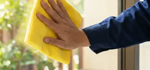 House cleaner wiping a glass window with a yellow microfiber cloth for streak-free cleaning, Rochester, NY.